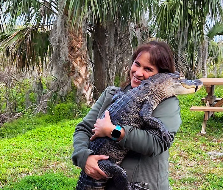 Columnist Fran smiling while holding an alligator, palm trees behind her